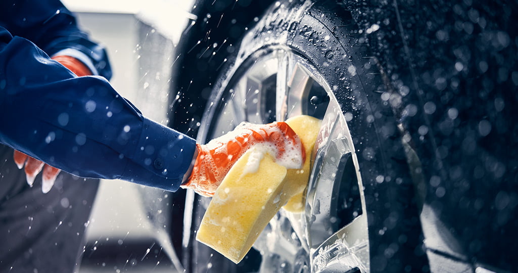 Vid en utvändig rekond tvättas bilen utvändigt. Person som rengör däcken på en bil.