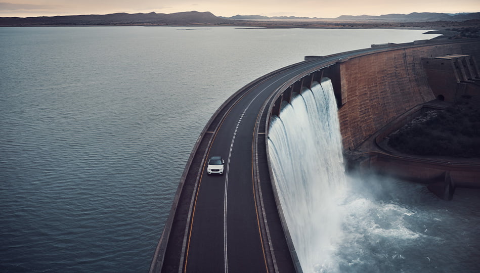 Vit Volvo XC40 Recharge som kör på bro över vattendamm