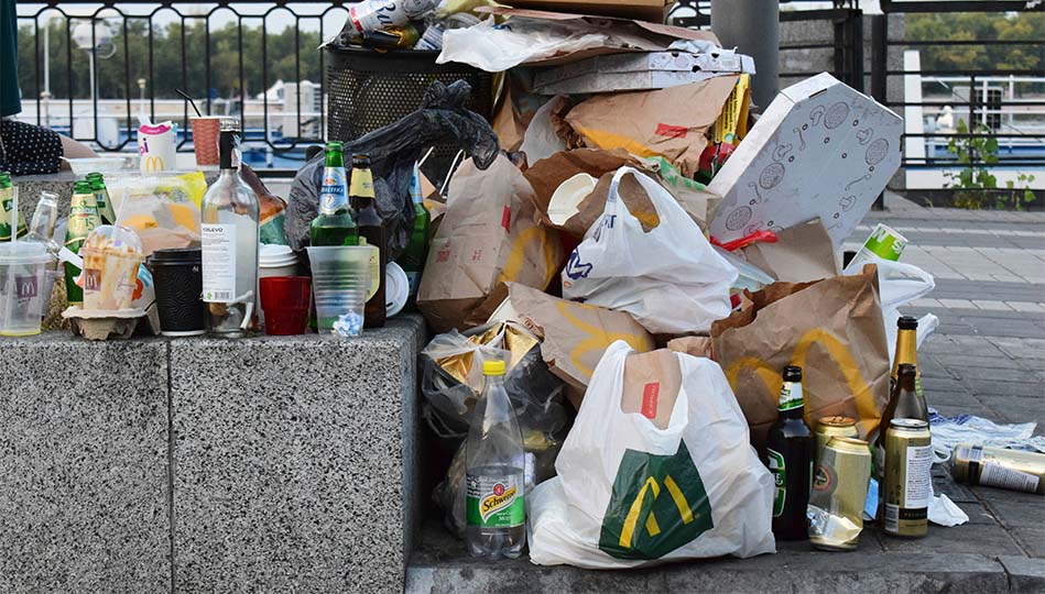 Överfull soptunna och flera påsar, lådor och flaskor som står utanför på trottoaren. Ser ut som att någon har städat bilen.