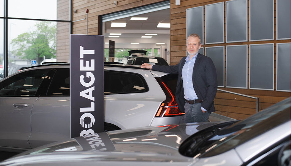 Fredrik Reuterby på Bilbolaget i Uppsala, står bredvid en skylt med Bilbolagets logotyp där enbart "Bolaget" syns