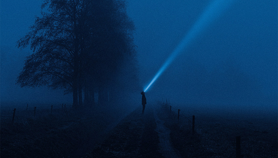 Person som lyser med en ficklampa rakt upp i luften en dimmig kväll.