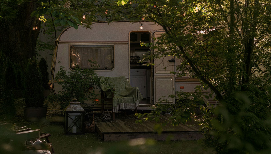 Äldre husvagn som står i en lummig skogsglänta.