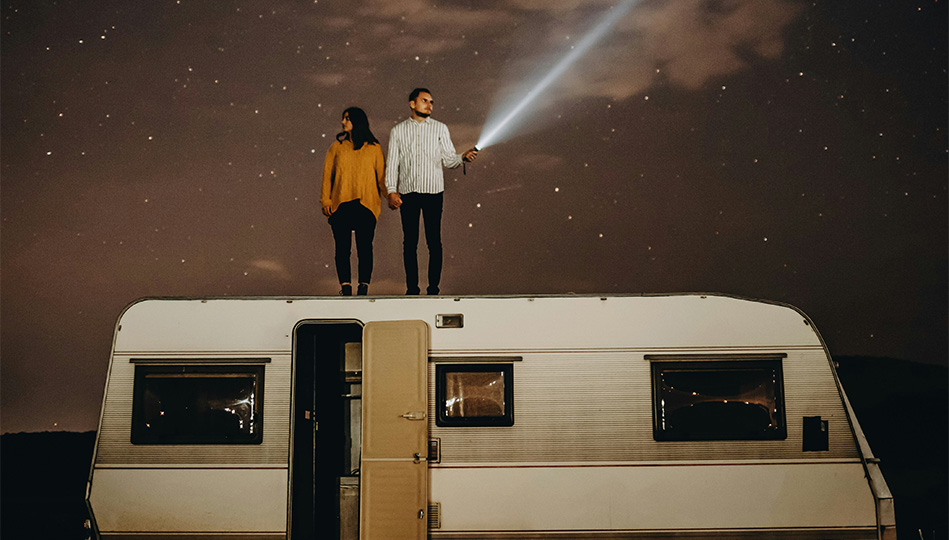 Par som står på taket av sin husvagn och lyser med en ficklampa ut i natten.